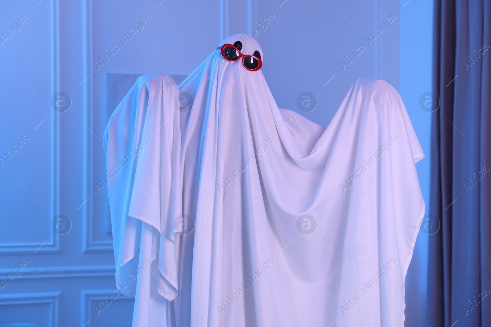 Funny ghost. Man covered with white sheet in blue light at home Photo of Funny ghost. Man covered with white sheet in blue light at home