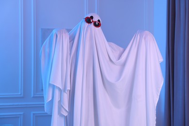 Photo of Funny ghost. Man covered with white sheet in blue light at home