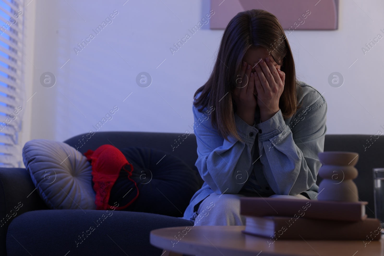 Photo of Betrayal. Frustrated wife covering face with hands and mistress bra on sofa at home