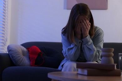 Photo of Betrayal. Frustrated wife covering face with hands and mistress bra on sofa at home