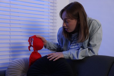 Photo of Betrayal. Shocked wife finding mistress bra near sofa at home