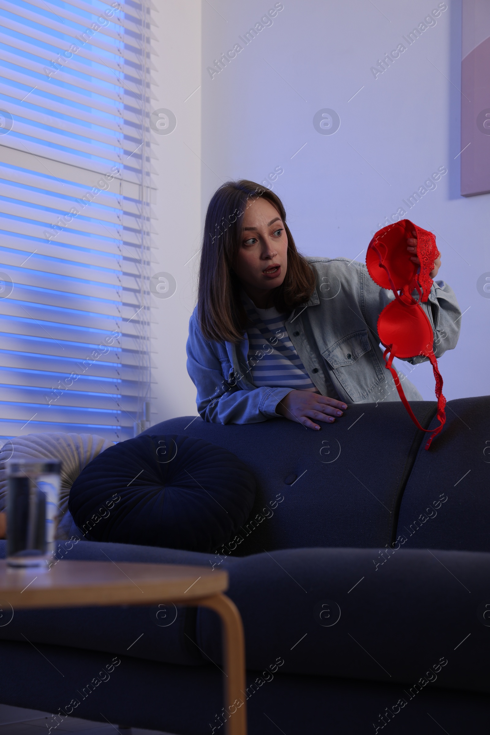Photo of Betrayal. Shocked wife finding mistress bra near sofa at home