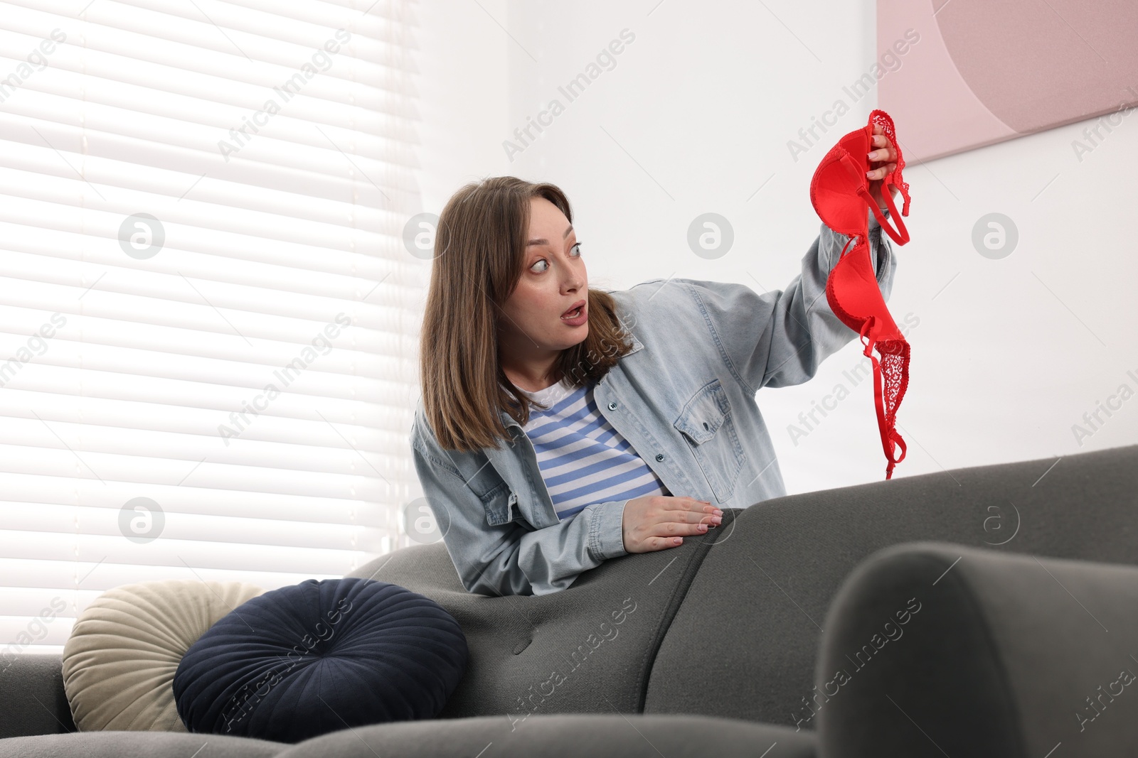 Photo of Betrayal. Shocked wife finding mistress bra near sofa at home