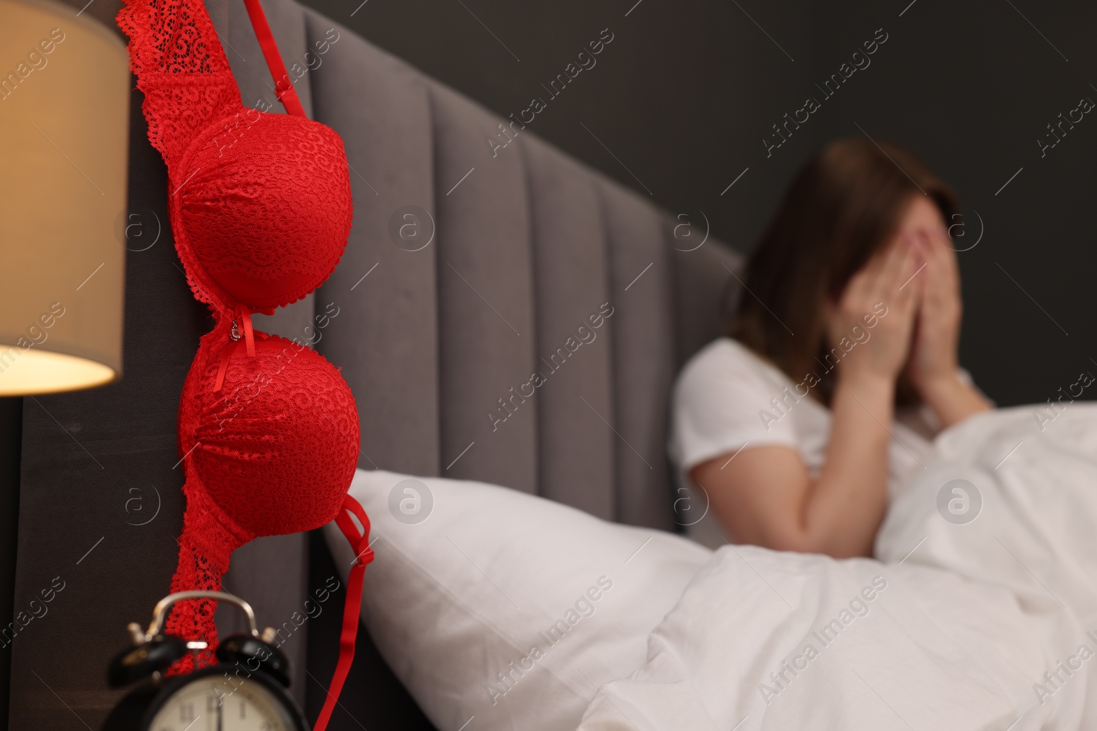 Photo of Betrayal. Frustrated wife covering face with hands on bed, focus on mistress bra