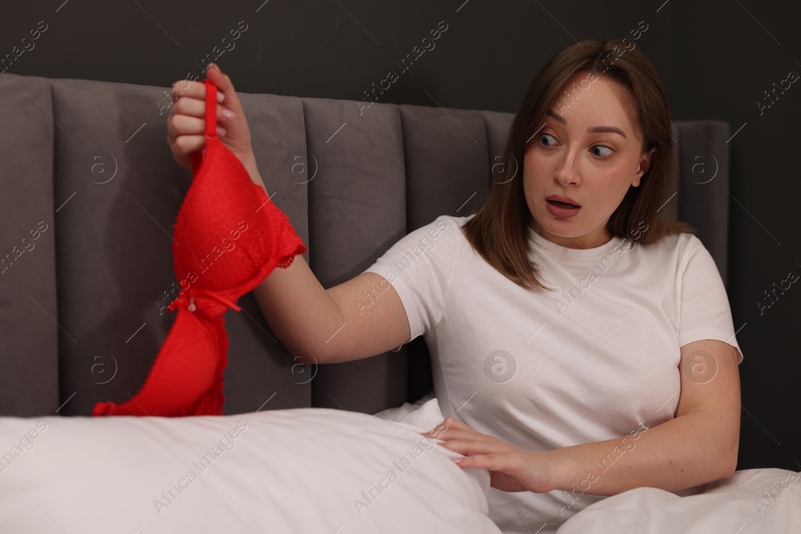 Photo of Betrayal. Shocked wife finding mistress bra on bed at home