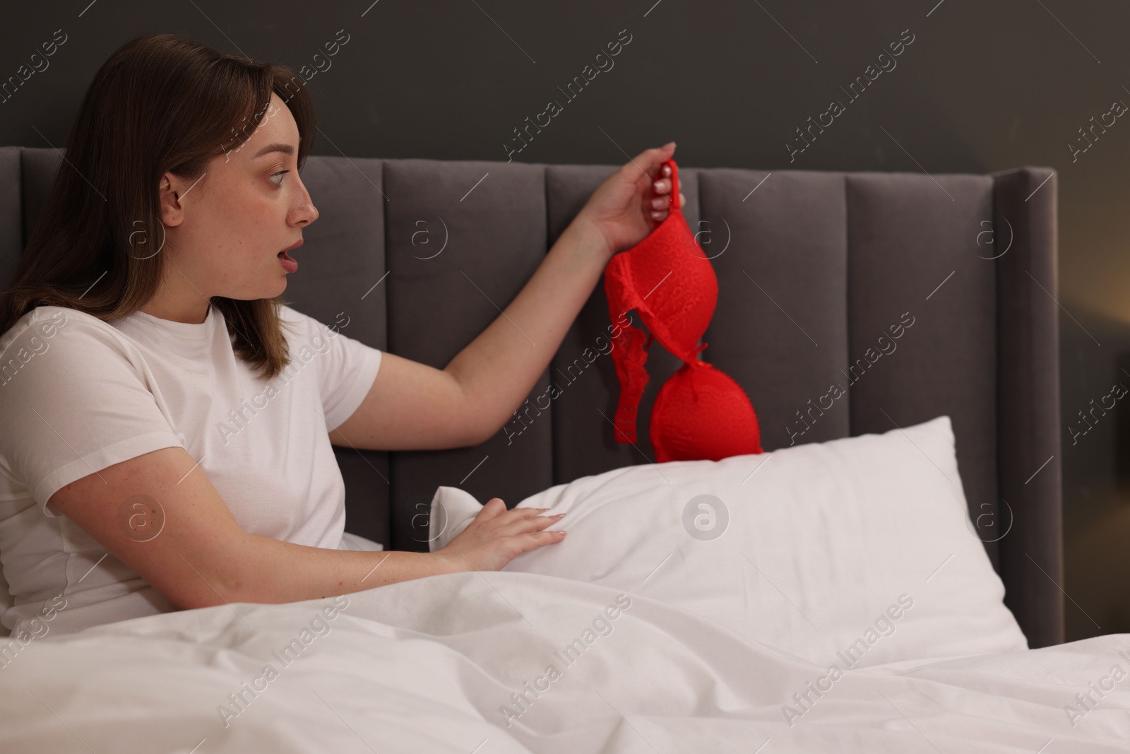 Photo of Betrayal. Shocked wife finding mistress bra on bed at home