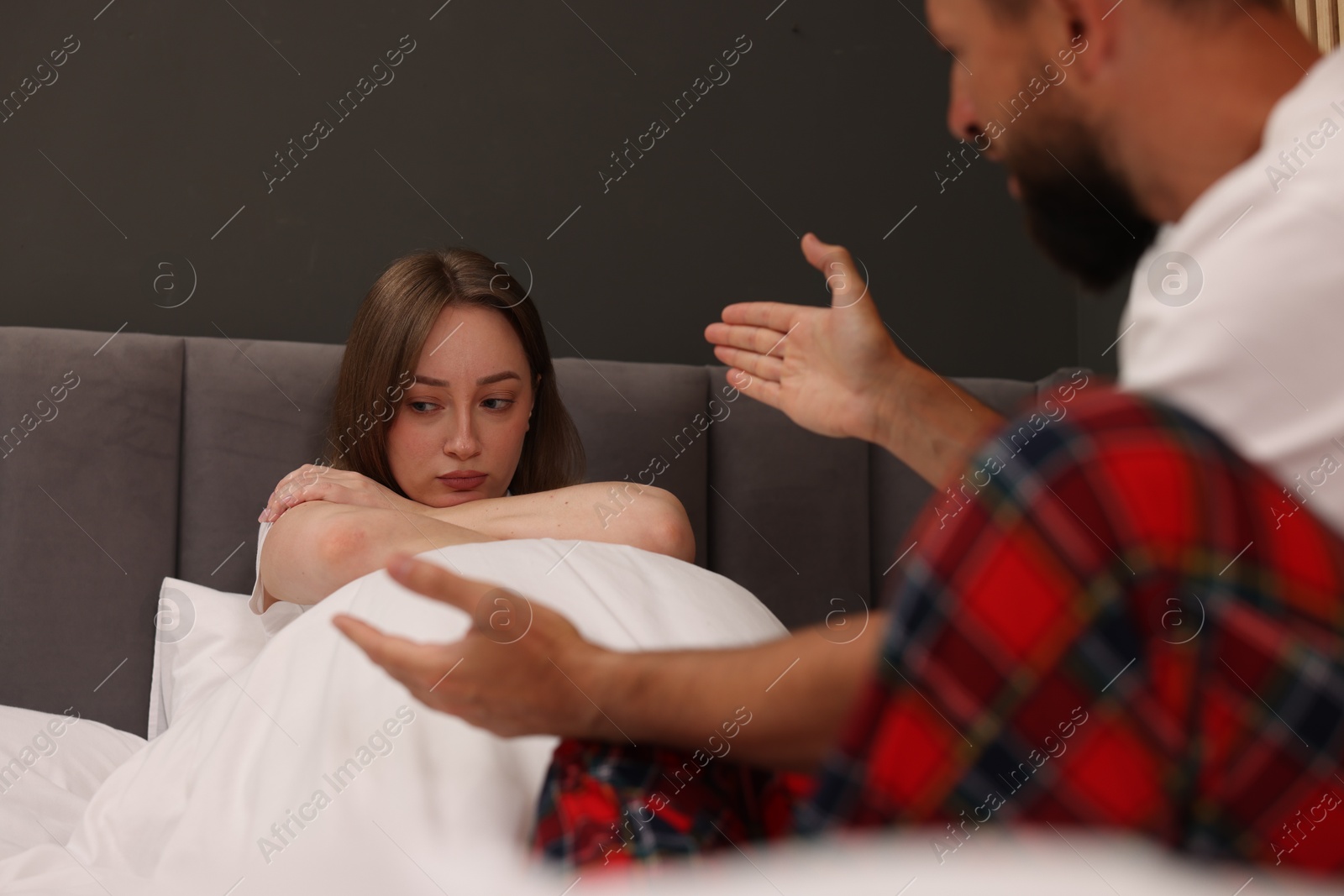 Photo of Betrayal. Upset woman ignoring her husband on bed at home, selective focus
