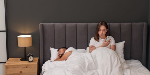 Photo of Betrayal. Jealous woman finding proofs of her unfaithful husband on smartphone while he sleeping in bed at home