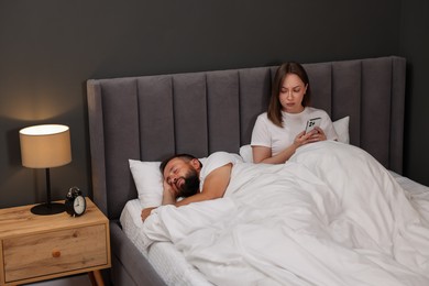 Photo of Betrayal. Jealous woman finding proofs of her unfaithful husband on smartphone while he sleeping in bed at home