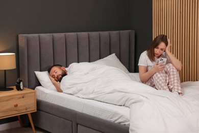 Photo of Betrayal. Frustrated woman finding proofs of her unfaithful husband on smartphone while he sleeping on bed at home