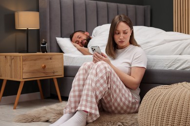 Photo of Betrayal. Frustrated woman finding proofs of her unfaithful husband on smartphone while he sleeping in bed at home