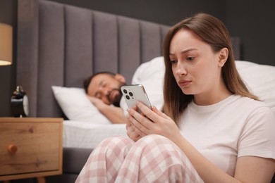 Photo of Betrayal. Frustrated woman finding proofs of her unfaithful husband on smartphone while he sleeping on bed at home, selective focus