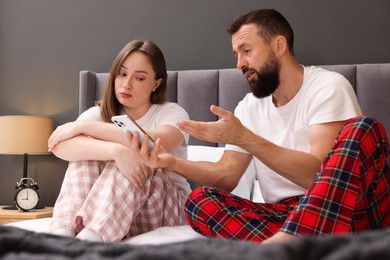 Photo of Betrayal. Husband showing smartphone with proofs to his unfaithful wife on bed at home