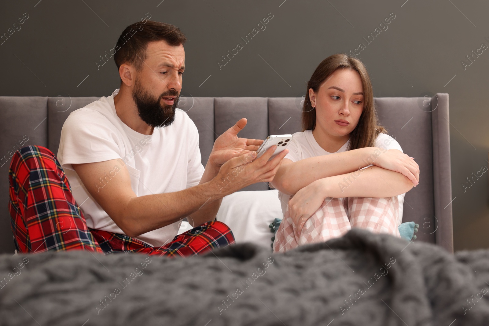 Photo of Betrayal. Husband showing smartphone with proofs to his unfaithful wife on bed at home