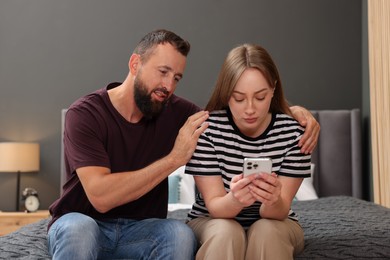 Photo of Betrayal. Couple looking at smartphone on bed at home