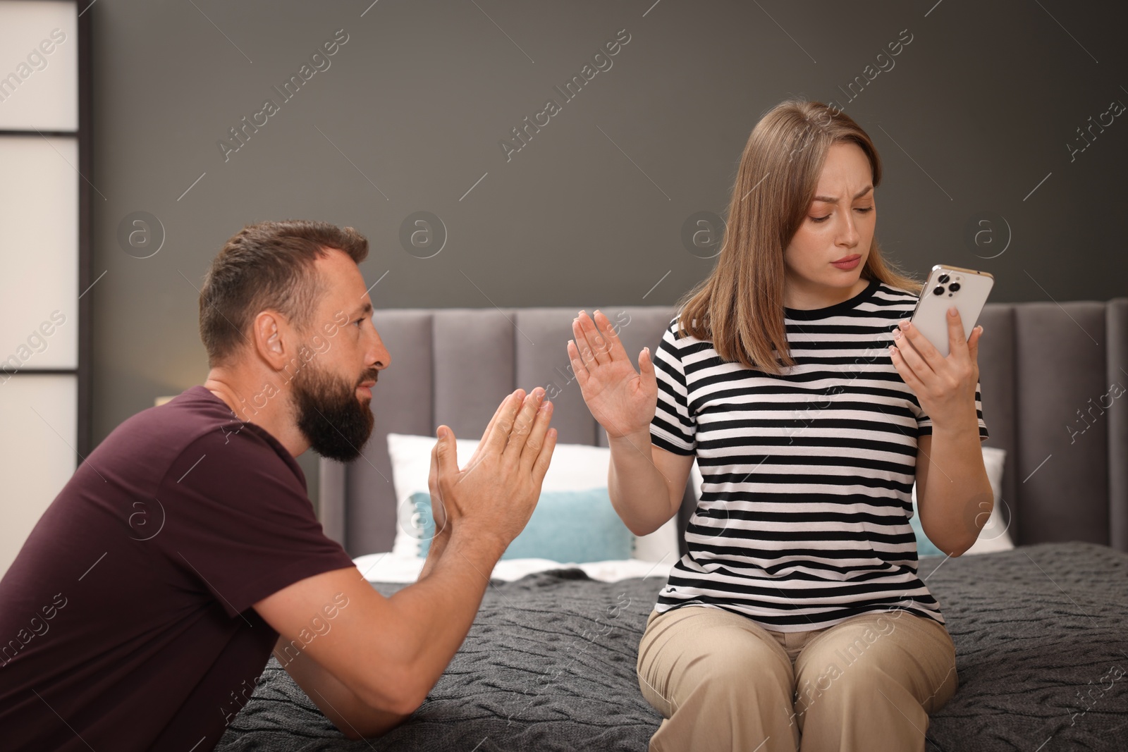 Photo of Betrayal. Husband apologizing to his offended wife while she stopping him on bed at home