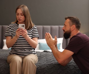 Photo of Betrayal. Husband apologizing to his offended wife on bed at home