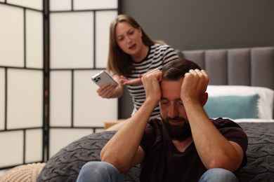 Photo of Betrayal. Angry woman with smartphone shouting at her offended husband on bed at home, selective focus