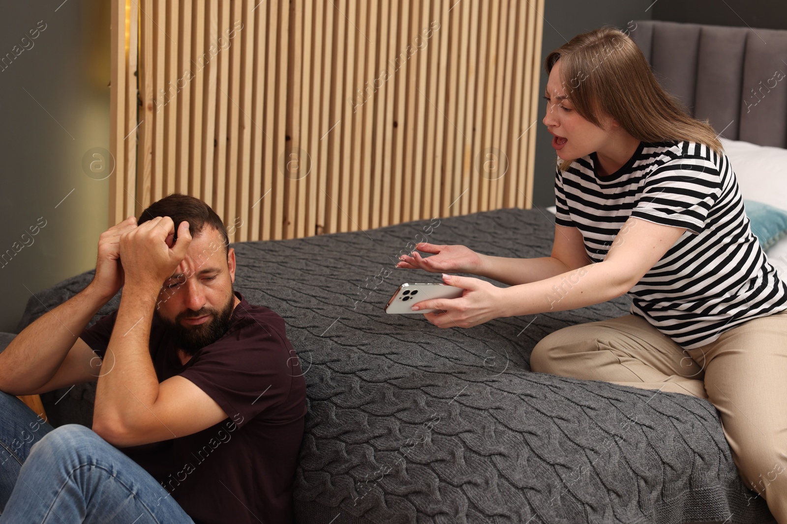 Betrayal. Angry woman with smartphone shouting at her offended husband on bed at home Photo of Betrayal. Angry woman with smartphone shouting at her offended husband on bed at home