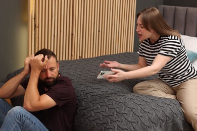 Photo of Betrayal. Angry woman with smartphone shouting at her offended husband on bed at home