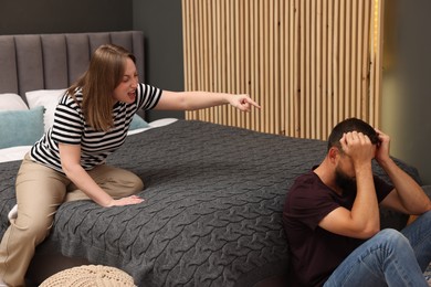 Photo of Betrayal. Angry woman shouting at her husband on bed at home
