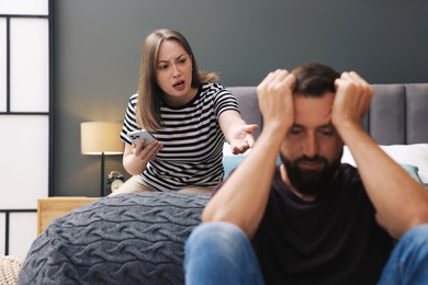 Photo of Betrayal. Angry woman with smartphone shouting at her offended husband on bed at home, selective focus