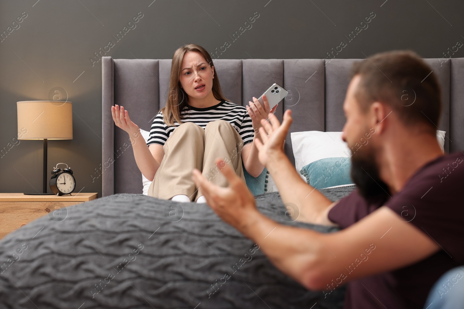 Betrayal. Angry woman with smartphone shouting at her husband on bed at home, selective focus Photo of Betrayal. Angry woman with smartphone shouting at her husband on bed at home, selective focus