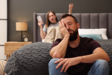 Photo of Betrayal. Angry woman with smartphone shouting at her tired husband on bed at home, selective focus
