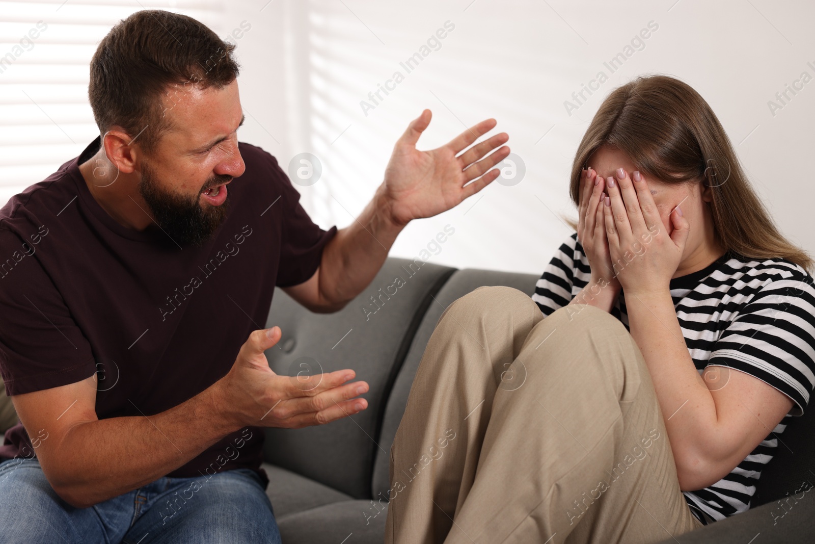 Photo of Betrayal. Angry man shouting at his frustrated wife on sofa at home