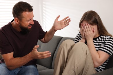 Photo of Betrayal. Angry man shouting at his frustrated wife on sofa at home