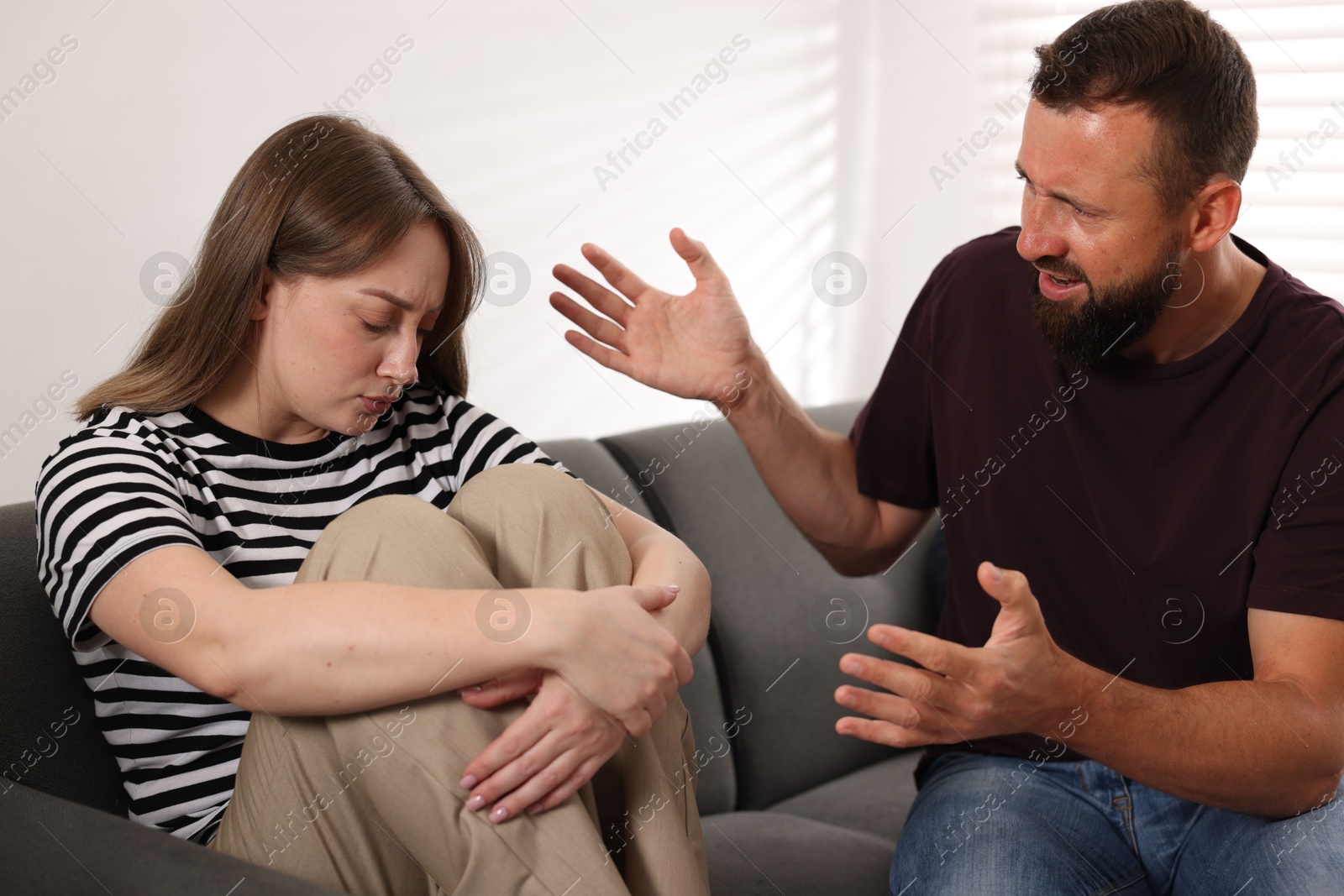 Photo of Betrayal. Angry man shouting at his frustrated wife on sofa at home