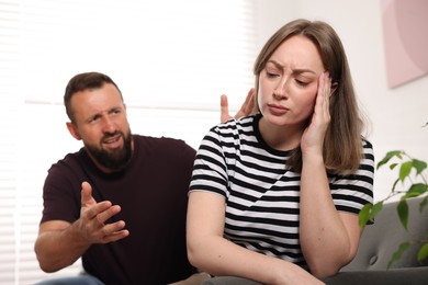 Photo of Betrayal. Angry man shouting at his frustrated wife on sofa at home