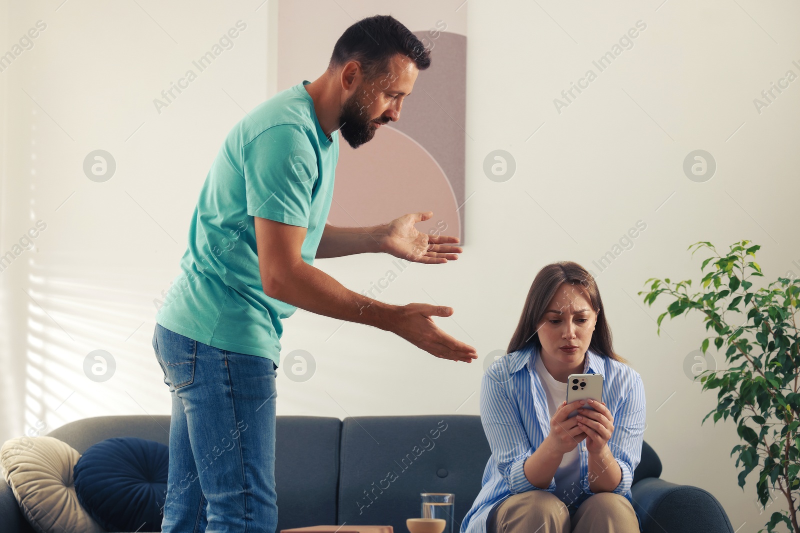 Betrayal. Offended wife with smartphone ignoring her husband on sofa at home Photo of Betrayal. Offended wife with smartphone ignoring her husband on sofa at home