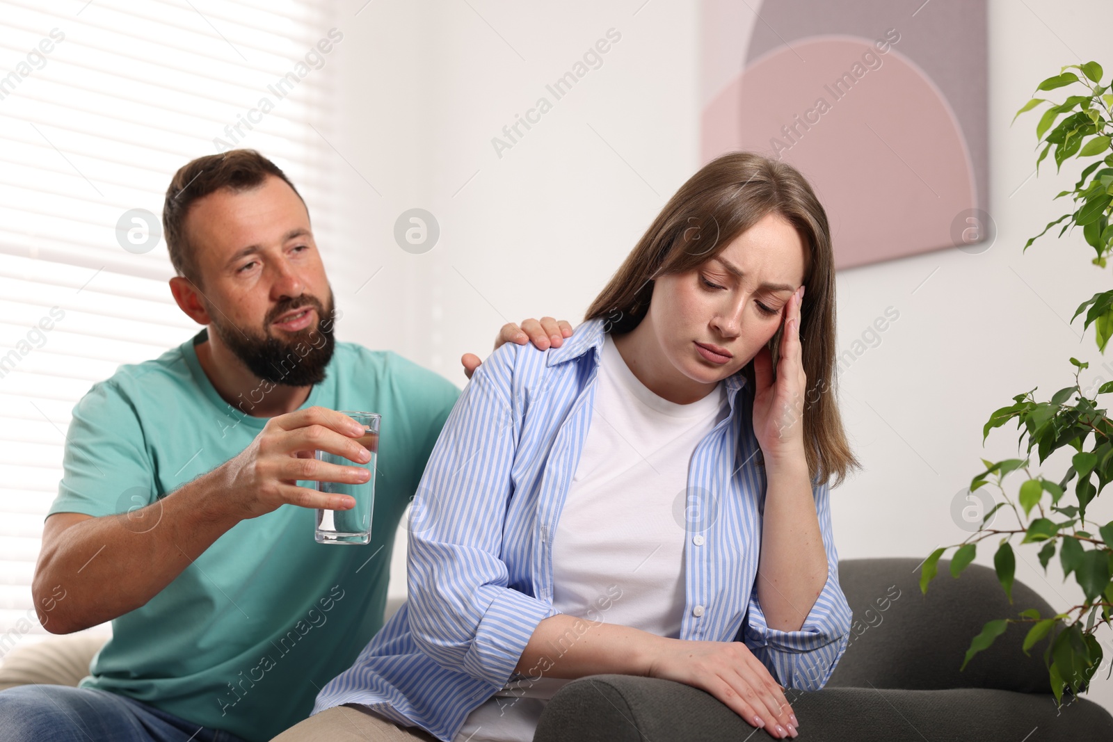 Betrayal. Husband with glass of water apologizing to his offended wife on sofa at home Photo of Betrayal. Husband with glass of water apologizing to his offended wife on sofa at home
