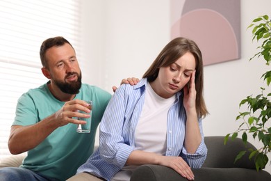 Photo of Betrayal. Husband with glass of water apologizing to his offended wife on sofa at home
