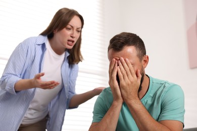 Photo of Betrayal. Angry woman shouting at her frustrated husband at home, selective focus