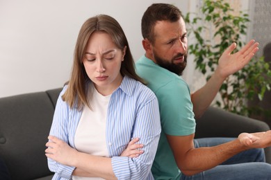 Photo of Betrayal. Upset woman ignoring her husband on sofa at home