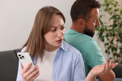 Photo of Betrayal. Woman with smartphone talking to her husband at home