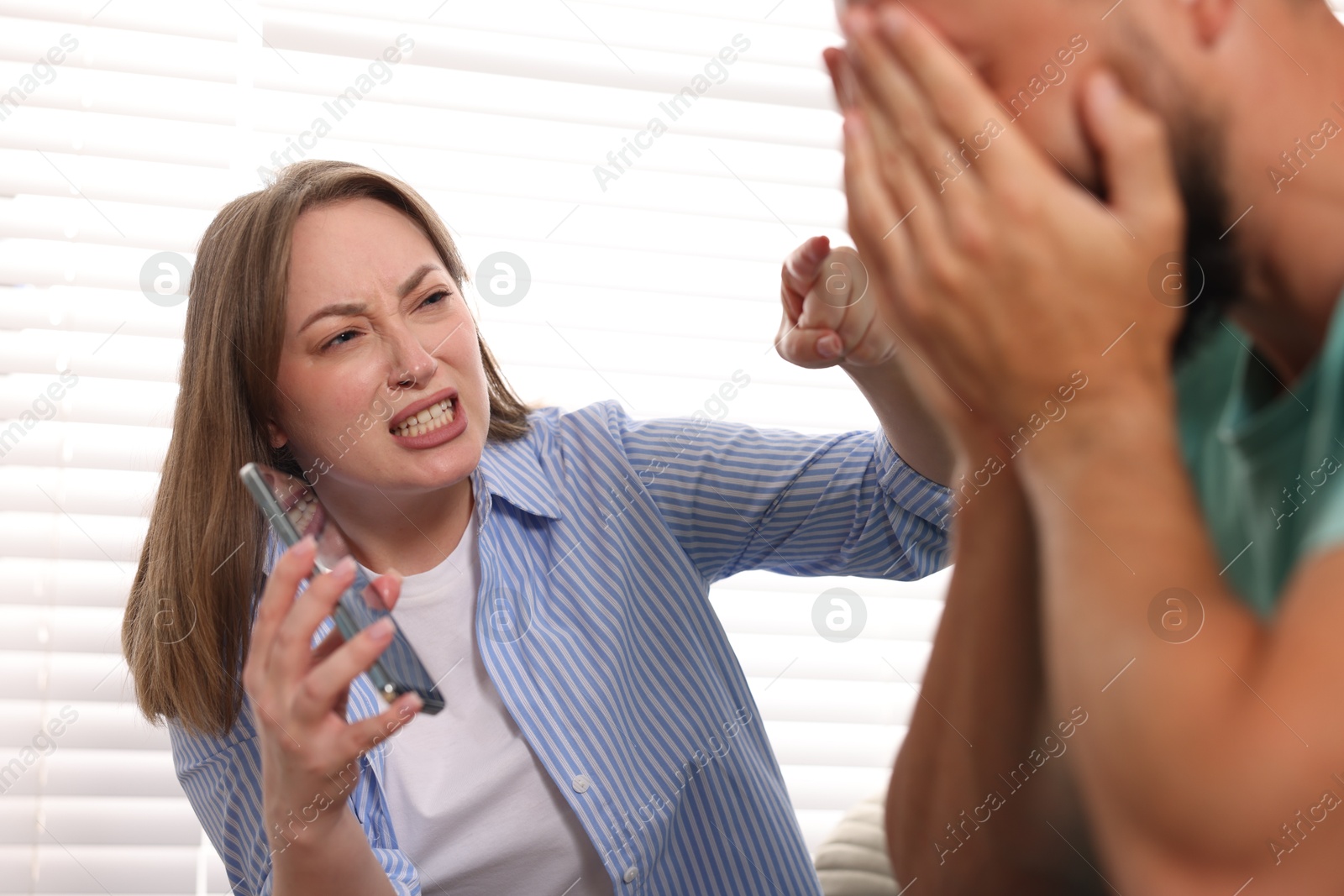 Betrayal. Emotional wife showing smartphone with proofs to her unfaithful husband at home, selective focus Photo of Betrayal. Emotional wife showing smartphone with proofs to her unfaithful husband at home, selective focus