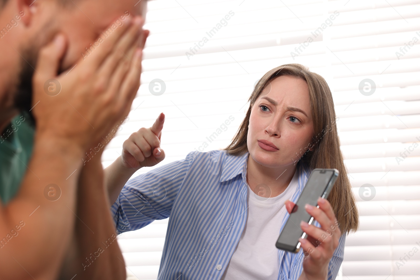 Betrayal. Emotional wife showing smartphone with proofs to her unfaithful husband at home, selective focus Photo of Betrayal. Emotional wife showing smartphone with proofs to her unfaithful husband at home, selective focus