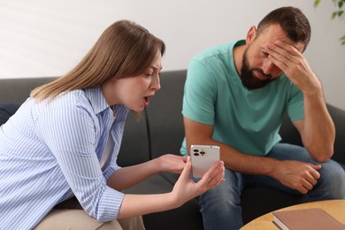 Photo of Betrayal. Emotional wife showing smartphone with proofs to her unfaithful husband on sofa at home