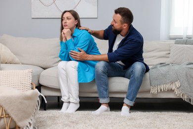 Photo of Betrayal. Husband apologizing to his offended wife on sofa at home