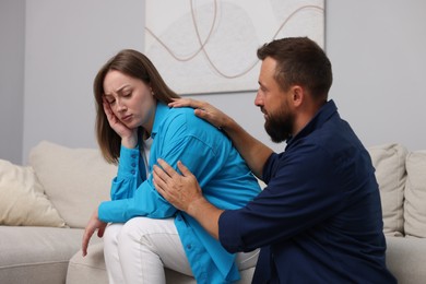 Photo of Betrayal. Husband apologizing to his offended wife on sofa at home