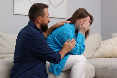 Photo of Betrayal. Husband apologizing to his crying wife on sofa at home