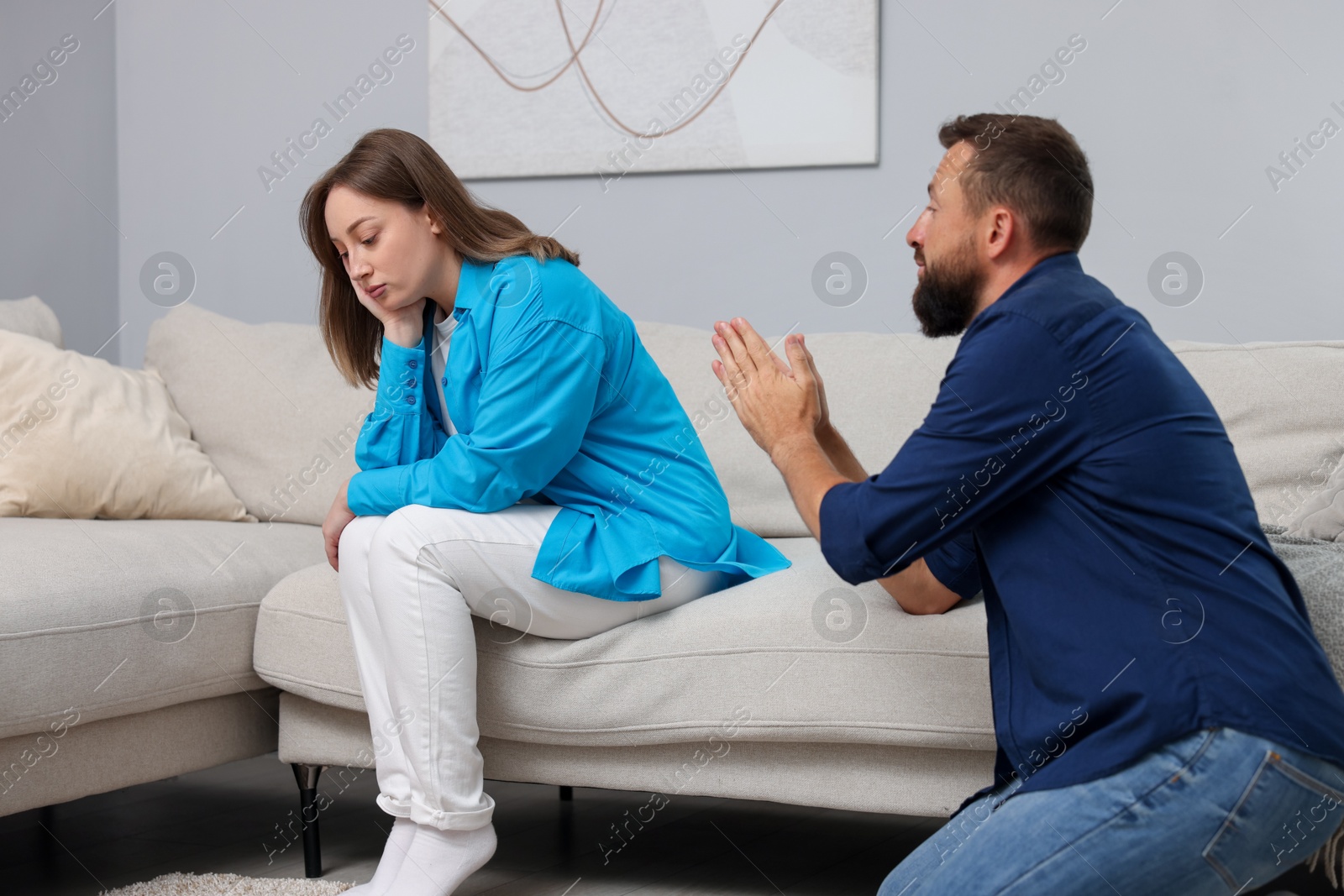 Photo of Betrayal. Husband apologizing to his offended wife on sofa at home