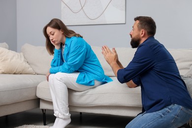 Photo of Betrayal. Husband apologizing to his offended wife on sofa at home