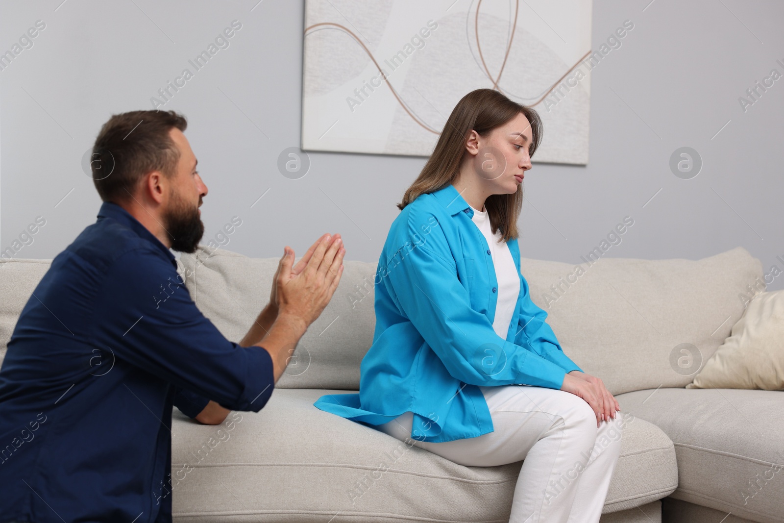 Photo of Betrayal. Husband apologizing to his offended wife on sofa at home