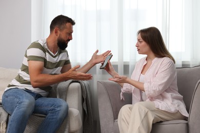 Photo of Betrayal. Wife showing smartphone with proofs to her unfaithful husband on sofa at home