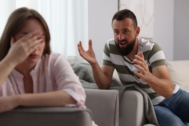 Photo of Betrayal. Angry man shouting at his offended wife on sofa at home, selective focus