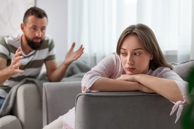 Photo of Betrayal. Man talking to his offended wife on sofa at home, selective focus